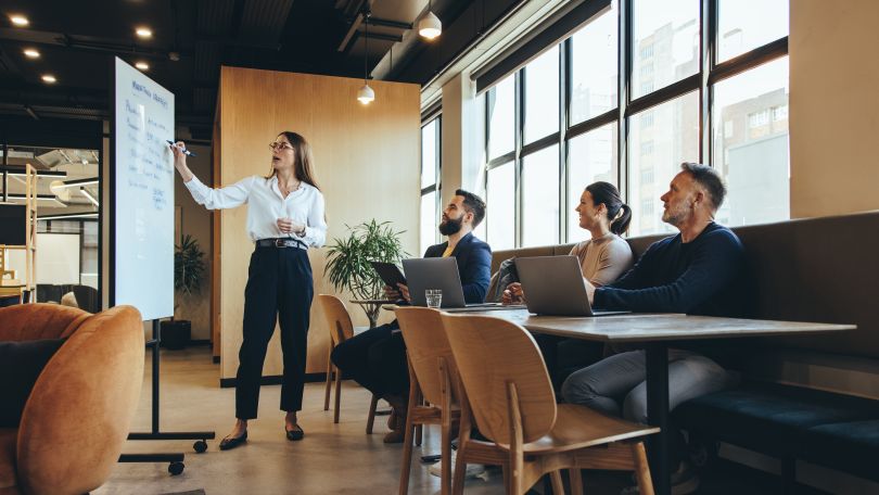 A person presenting to a small group using a white board